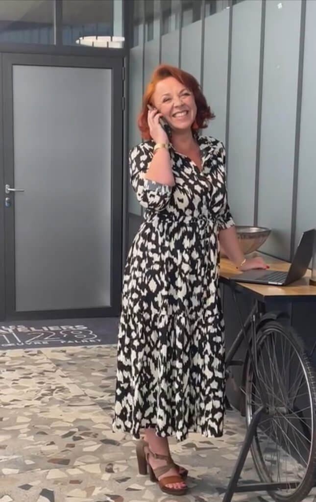 La Rebelle du Web, Sabine, se tient debout avec un grand sourire, le téléphone à la main et son ordinateur, à côté posé sur un magnifique bureau vintage